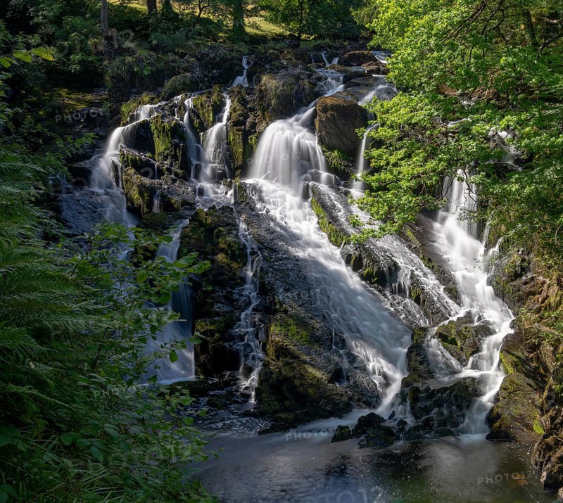 A view of the Swallow Falls waterfall in Anglesey in northern Wales surrounded by lush green summer vegetation