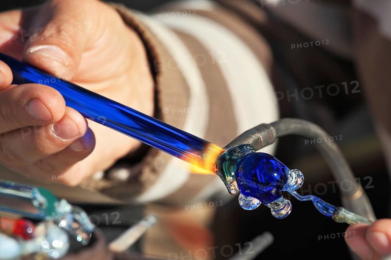 Delicate work of the glass blower. On a photo hands of the master are visible. The Artist-glass blower produces a graceful tiny figure of an elephant from color glass