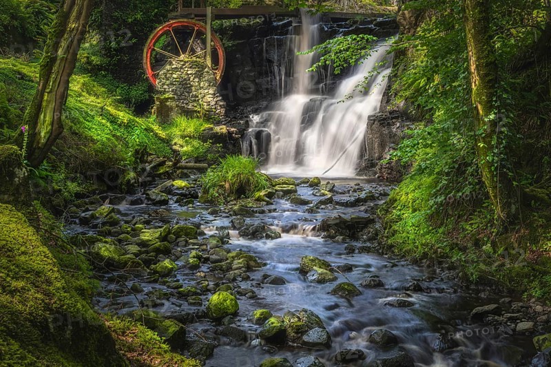 Stream leading to red waterwheel and waterfall in Glenariff Forest Park, County Antrim, Northern Ireland. Long exposure and soft focus photography