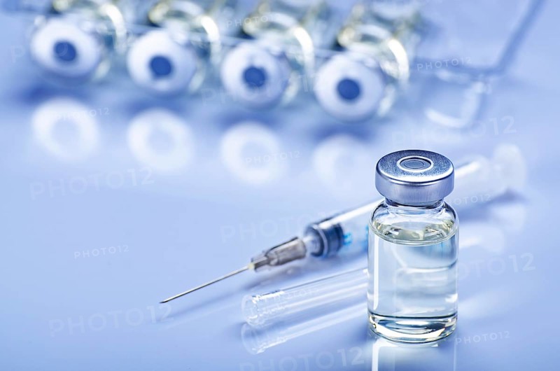 Single use syringe for injection treatment on medical table with vials of liquid drug doses flu shots at background. Vaccination or immunization care concept
