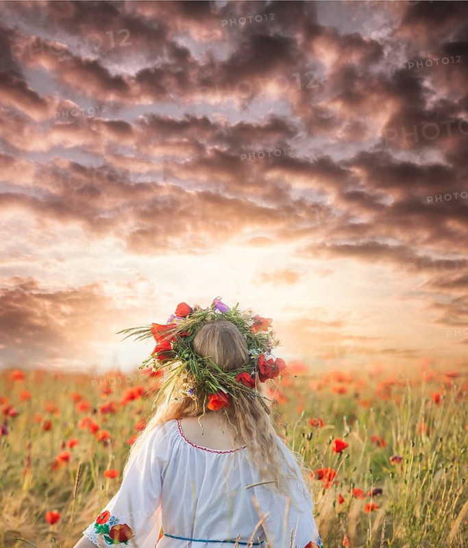 Pretty blonde girl in a dress with a pattern poppy and with a wreath on his head enjoying in a field with poppies. View from the back, copy space for inspired text