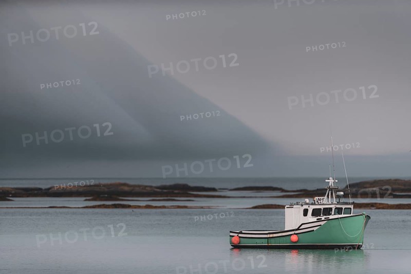 A commercial fishing boat sits tied to its mooring with dramatic clouds above, behind it are shoals leading to the Atlantic Ocean in Lunenburg, Nova Scotia, Canada, North America