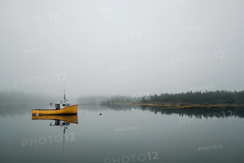 A commercial fishing boat is reflected in the still calm water of a protected bay as light fog begins to cover the shoreline in Lunenburg, Nova Scotia, Canada, North America