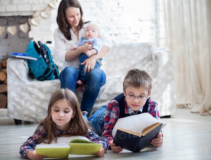 Son and daughter with their mother and little brother siting on the sofa. Children readind books in living room. Focus on the children