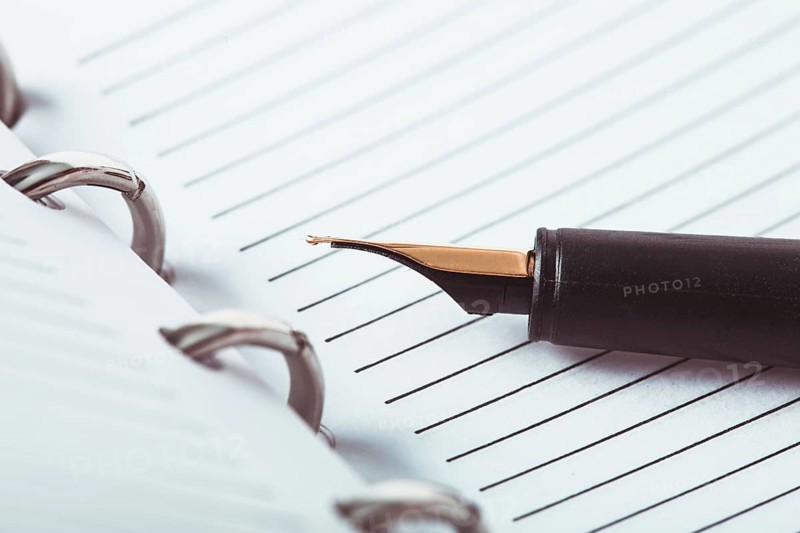 Metal feather pen on the ruled paper in the notebook