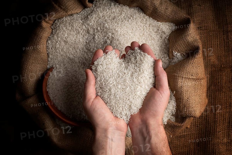 Human hands in shape of heart holding handful of rice over burlap sack