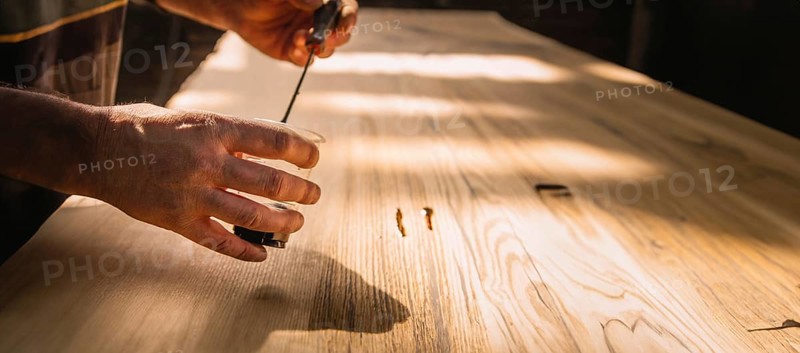 Close-up of hands working on a wooden tabletop, with sunlight creating a serene working environment