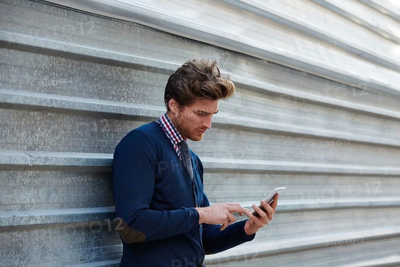 Young businessman texting smartphone phone on the street metal fence
