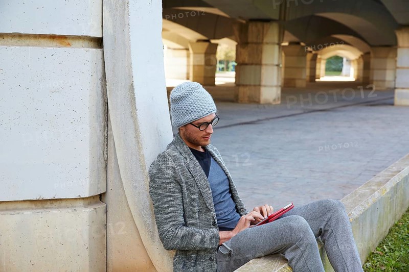 Modern young man with tablet pc touch working under a bridge with wool winter cap