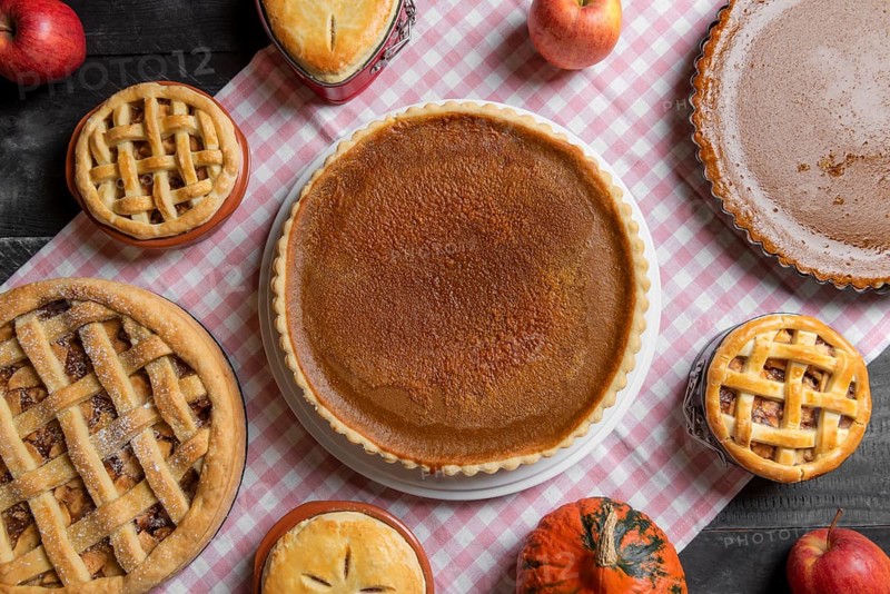 Above view of a table with a pink towel, full of various homemade pies, pumpkin pies, apple pies, raspberry pies. Traditional sweet food baking
