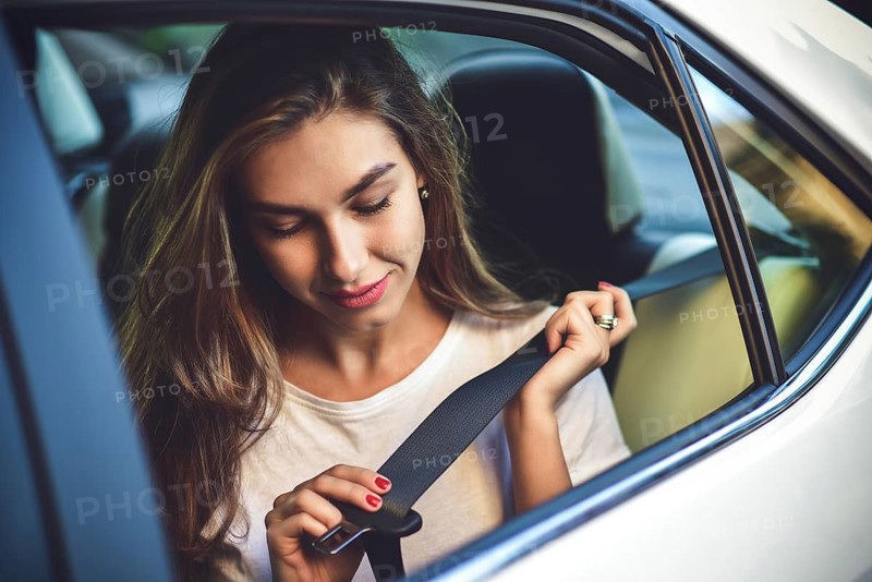 Beautiful woman with phone smiling while sitting on the back seat in the car