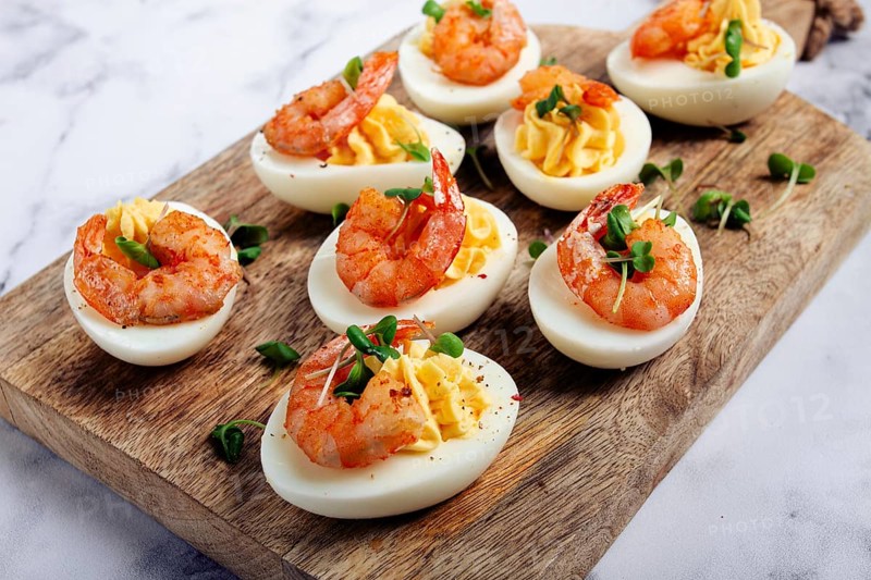 Boiled eggs stuffed with yolk and seasoned with mayonnaise, stuffed eggs with shrimp, on a wooden chopping board, selective focus, close-up, no people