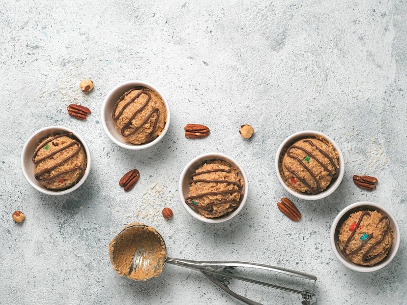 Safe-to-eat raw monster cookie dough in small portion bowl, ice cream scoop and nuts on gray cement background. Ideas and recipes for kids and toddlers meal. Top view or flat-lay. Copy space for text