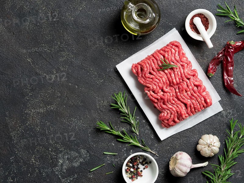 Fresh raw minced beef on backing paper and cutting board and ingredients over black cement background with copy space. Top view or flat-lay