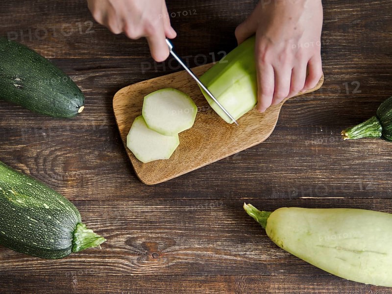 Zucchini harvest. Woman slices zucchini on wooden table. Farm organic zucchini harvesting