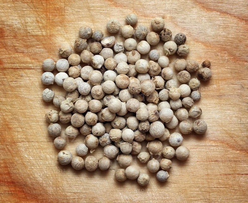 Spices, white pepper peppercorns macro on wooden board