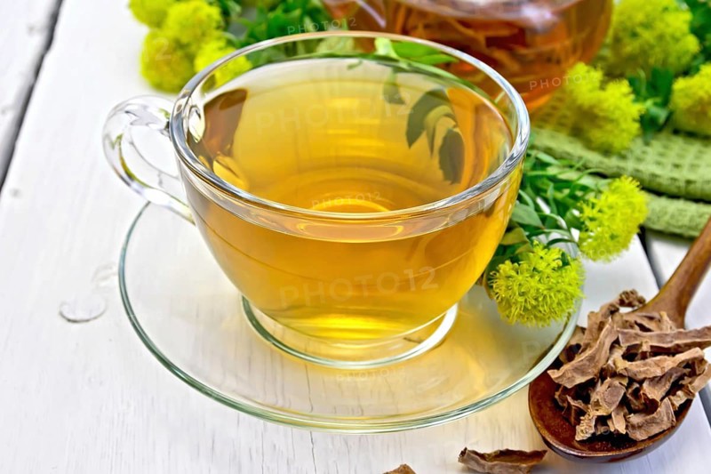 Herbal tea in a glass cup, a teapot on a napkin, spoon with dry roots of Rhodiola rosea, fresh flowers of Rhodiola Rosea on the background wooden boards
