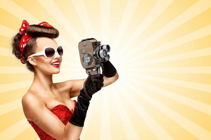 Glamorous pin up girl shooting a film with an old retro cinema 8mm camera on a colourful abstract cartoon style background