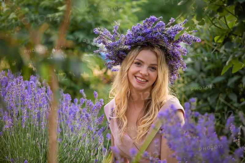 Blonde woman in wreath near lavender bushes at the garden