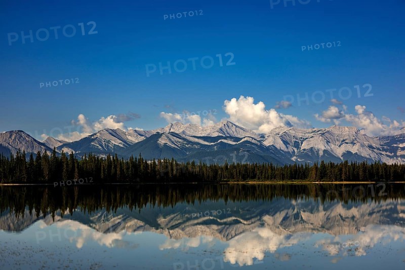 The Canadian Rockies and bright blue sky are reflected in a lake near Canmore, Alberta, Canada, North America