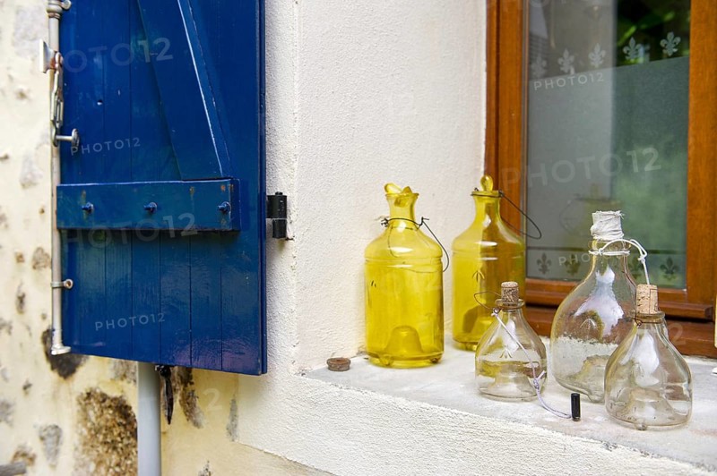 Still life with old glass bottles in window with blue shutters in France