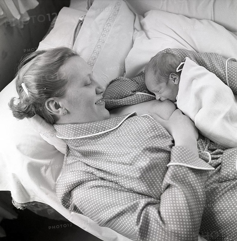 1950s mother nursing her baby. A young woman breastfeeding her baby while lying in bed at home. Sweden 1951 Neg CV/24