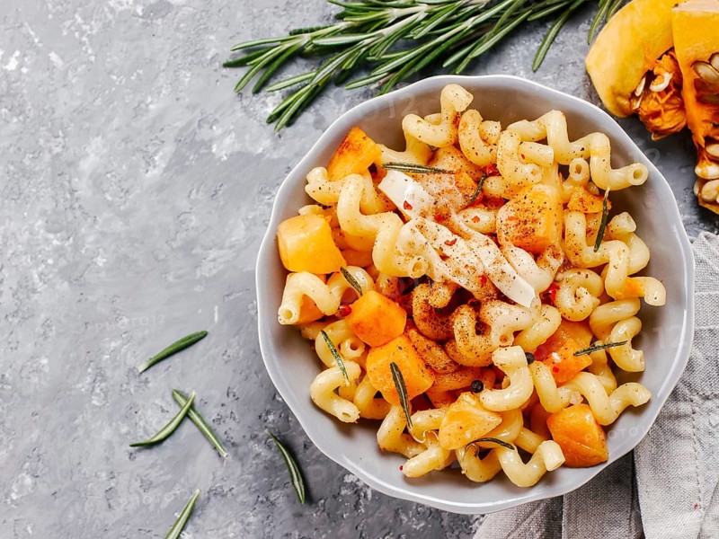 Fusilli pasta with pumpkin, rosemary and brie cheese. Idea recipe pasta. Vegetarian food. Homemade pasta dish in gray bowl over gray concrete background. Copy space. Top view or flat lay