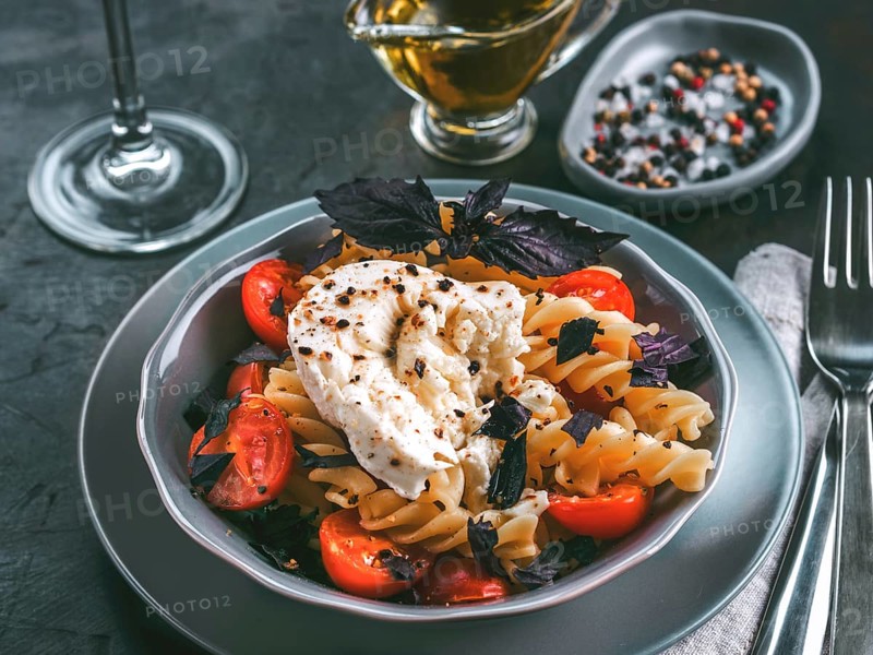 Tasty italian fusilli pasta with cherry, mozarella or buratta cheese and fresh basil. Dish with pasta on dark tabletop. Copy space. Healthy food concept and recipe idea