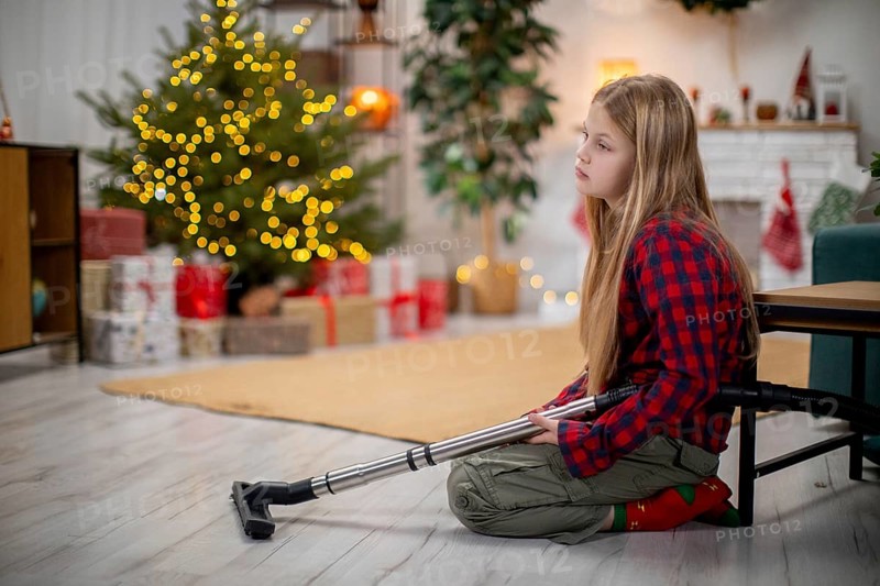 A thoughtful and reflective child who uses a crutch sits quietly beside a beautifully decorated Christmas tree