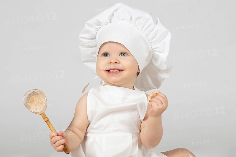 Child cooking. Beautiful little girl in cooking clothes with a big spoon. The child is one year old. Funny baby laughs. Little cook. The concept of cooking food