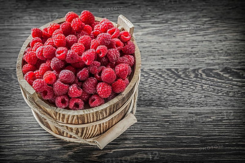 Red raspberry in bucket on vintage wooden board