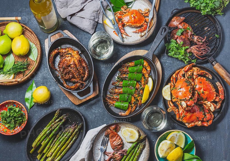Food, Food, Set table with seafood dishes, cooked crabs, tiger shrimps, grilled octopus and squids on cast iron grilled pans and plates, White wine. Toned photo. Top view