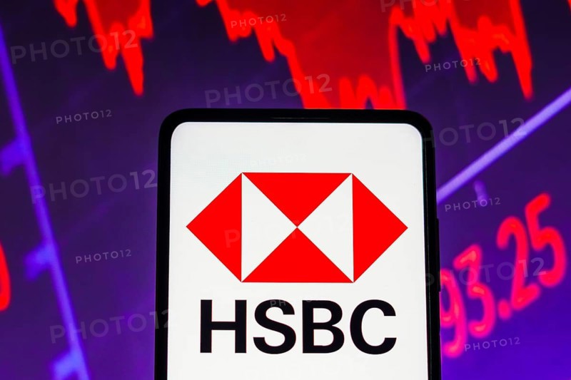 In this photo illustration the HSBC logo seen displayed on a smartphone screen, with graphic representation of the stock market in the background
