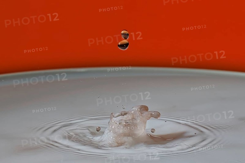 A beige water droplet hits the water surface and creates a small splash on an orange background, water droplets, collision, highspeed photography, concept, water figures