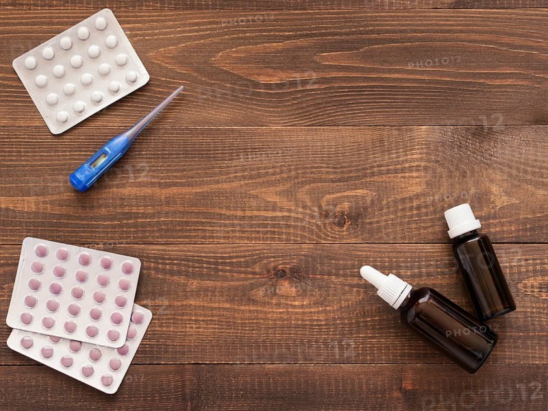 Medications or tablets and drops and electronic thermometer on a dark wooden background with copy space. Flat lay or top view