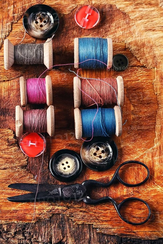 Six antiquated sewing threads and buttons on retro background