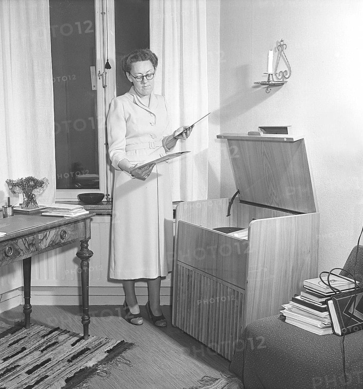 Woman at a gramophone in the 1940s. Dagmar Lange, swedish author, 1914-1991. Holding two records thinking of which she will play on the gramophone. On this model there were ways of modifying the sound in order to improve the listening experience. The records were made of fragile material and the speed of the record to sound as it should was 78 revolutions per minute. Sweden 1949. Kristoffersson ref AT17-3
