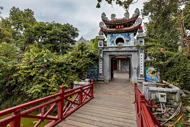 A richly decorated temple with a wooden walkway, surrounded by lush greenery and Asian architectural elements, the Ngoc Son Temple in Hoan Kiem Lake in Hanoi Vietnam