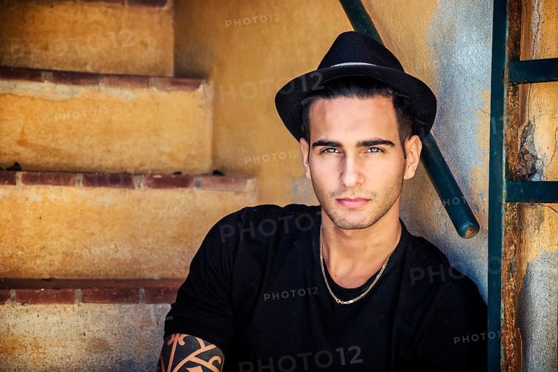 Portrait of handsome man with tattoo on hands sitting on cement stairs while leaning on wall