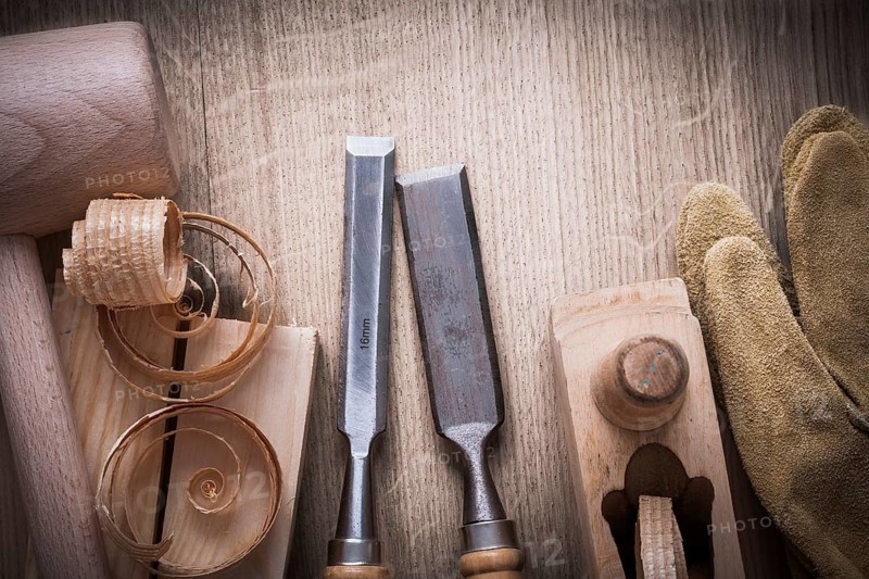 Wooden bricks mallet curled up shavings planer firmer chisels leather gloves on wood background construction concept