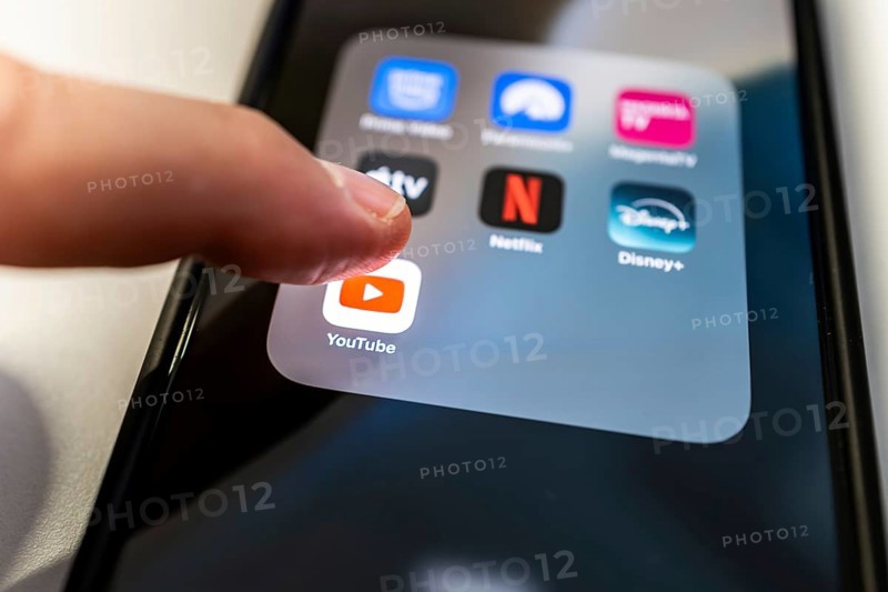 One finger touches the YouTube icon on a smartphone screen with various other streaming apps