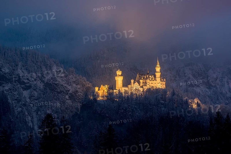 A mysteriously illuminated castle rises above a snow-covered forest in the evening mist, Neuschwanstein, Schwangau, Ostallgäu, Allgäu, Swabia, Upper Bavaria, Bavaria, Germany, Europe