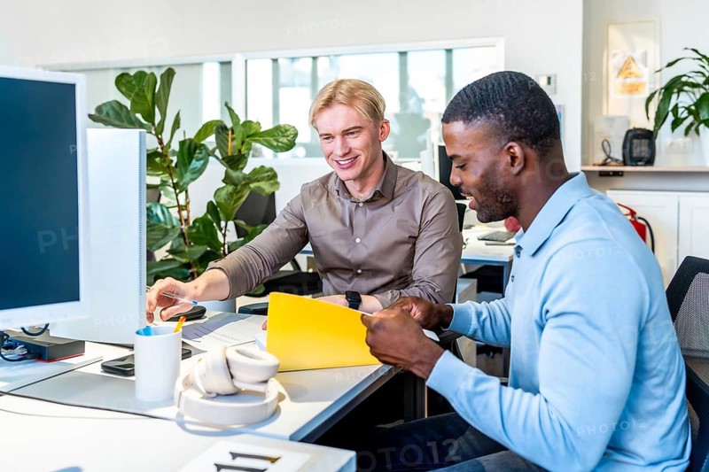 Two businessmen are working together in a coworking office, reviewing documents and collaborating on a project