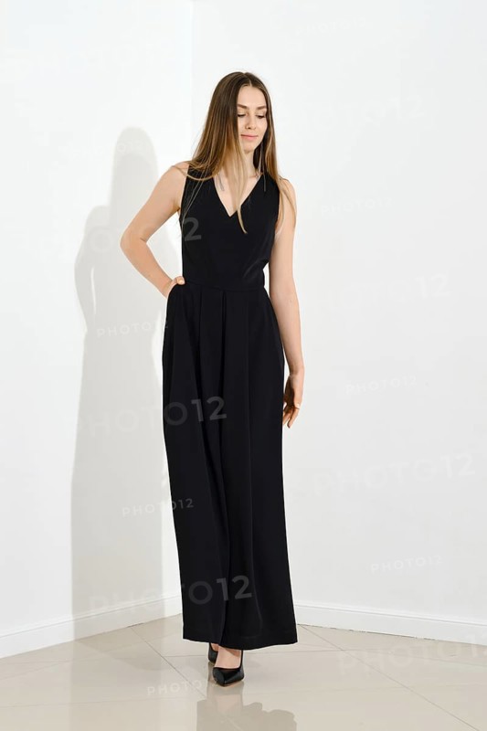 Cute lovely young woman in long sleeveless dress walking in bright room