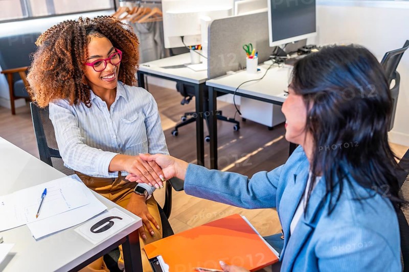 Two happy businesswomen shaking hands after a successful job interview in a modern coworking office