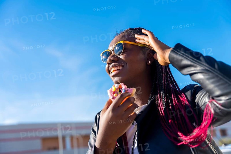 Low angle view photo of an african woman eating a multicolored doughnut in the street