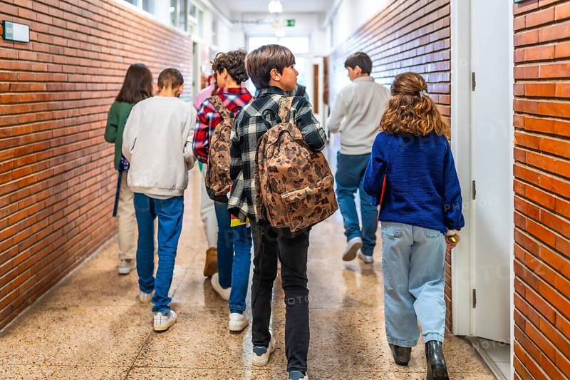 Group of elementary school students walking down school hallway between classes, carrying backpacks and books