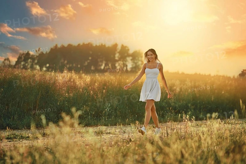 Happy young woman walking along country road in the meadow during sunset