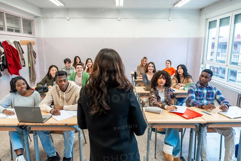 Female professor teaching a lesson to a multi ethnic group of students sitting at desks in a classroom