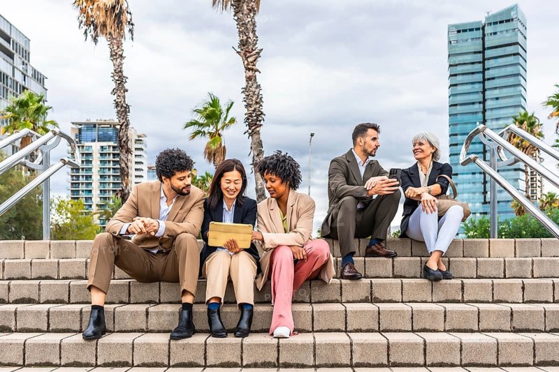 Multi-ethnic business people sitting in the street talking and using digital tablet together